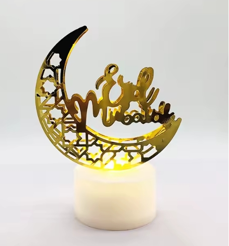 Decorative gold crescent moon with 'Eid Mubarak' on a white candle against a light Gray background